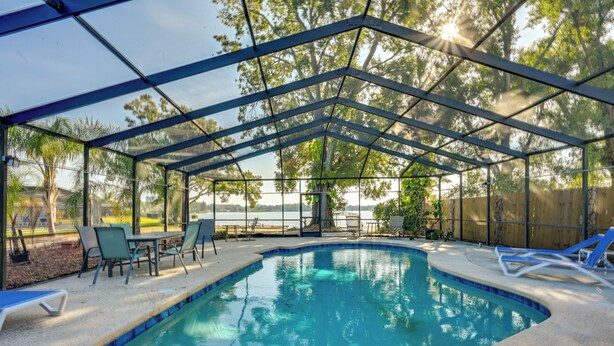 A covered swimming pool with lounge chairs and a table, surrounded by trees and a view of the outdoors. - Dock & Beautiful Views! Spacious Bellows Lake Gem (Tampa)
