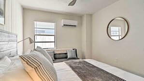 A bedroom with a bed, a bedside table, a lamp, a window with blinds, an air conditioner, and a mirror on the wall. - Well-appointed Madeira Beach Condo w/ Patio! (Madeira Beach)