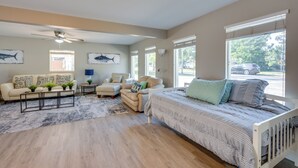 Un salon spacieux comprenant un canapé, un fauteuil et un lit. De nombreuses fenêtres laissent entrer la lumière naturelle et offrent une vue sur l’extérieur.