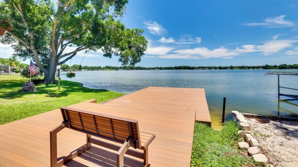 Une terrasse en bois avec un banc donnant sur un lac, entourée d’herbe et d’arbres.
