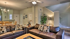 A living room with a brown leather sofa, a wooden coffee table, and a ceiling fan. - 5 Mi to Disney: Emerald Island Resort Condo! (Kissimmee)