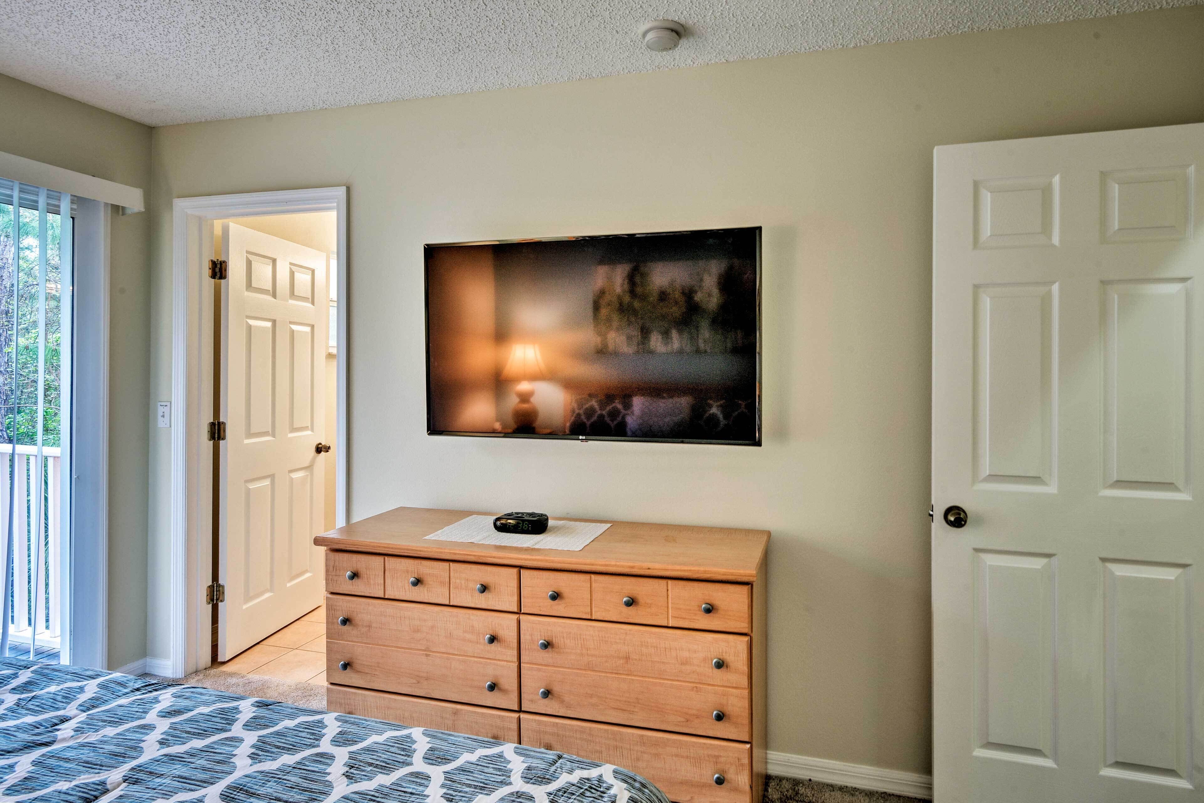 Een slaapkamer met een bed, een dressoir, een aan de muur bevestigde televisie en een deur aan de linkerkant.