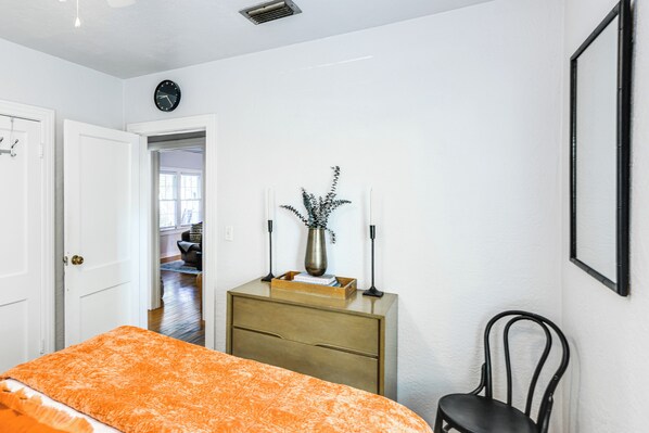Une chambre à coucher comprenant un lit, une commode, une chaise, une horloge et une porte donnant sur une autre pièce.