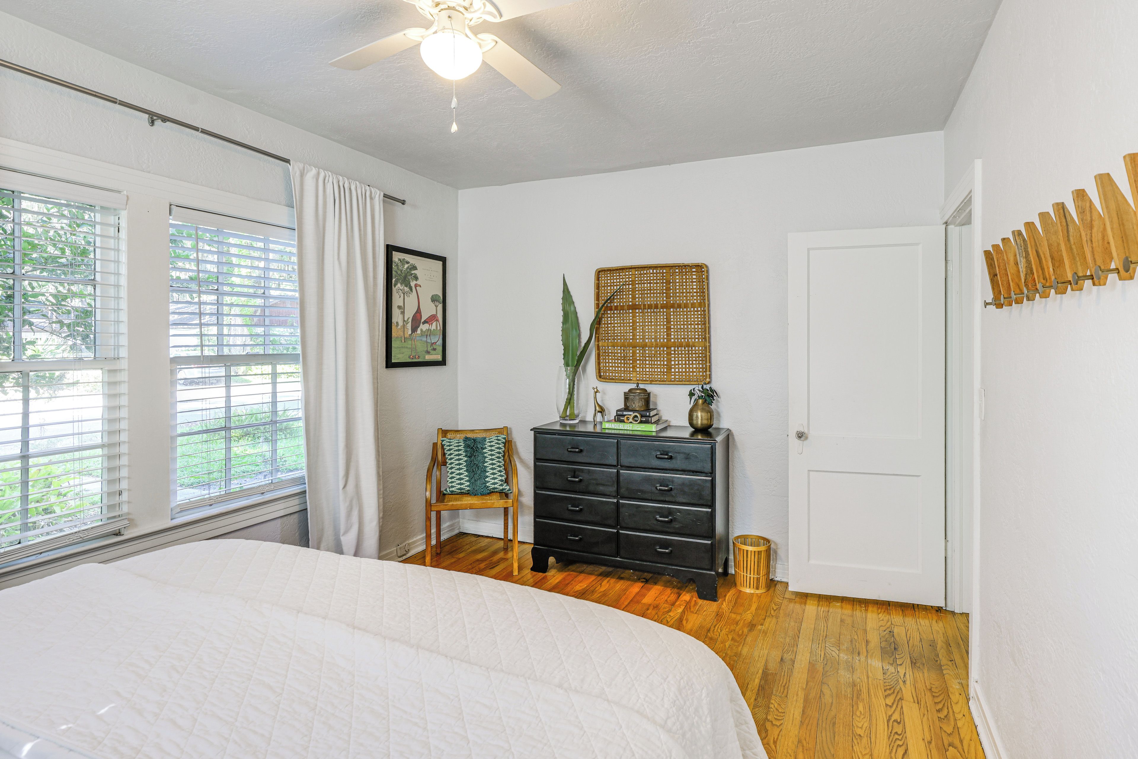 A bedroom with a bed, a dresser, a chair, a window with blinds, and a ceiling fan.