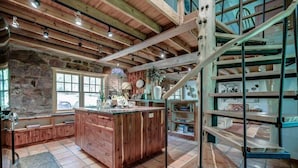 A rustic kitchen with a wooden island, stone walls, and a spiral staircase.