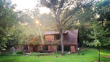 A rustic two-story house with a stone facade and a sloped roof, surrounded by a well-maintained lawn and trees.