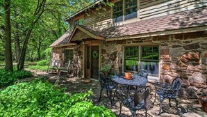 A rustic stone cabin with a patio, surrounded by lush greenery.