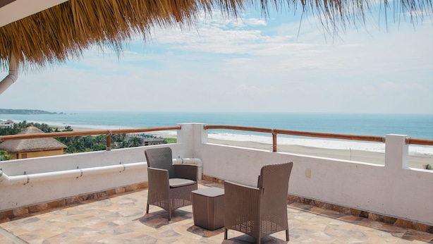 Un balcon meublé de mobilier en osier, donnant sur une plage.
