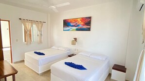 Une chambre d’hôtel avec deux lits, un ventilateur de plafond, un tableau et une petite table.