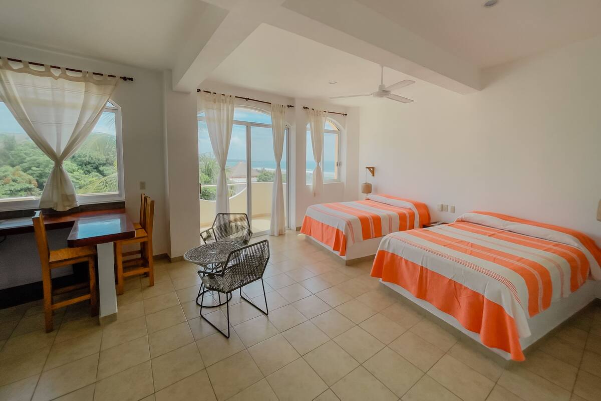 A room with two beds, a desk, a chair, and a view of the sea.