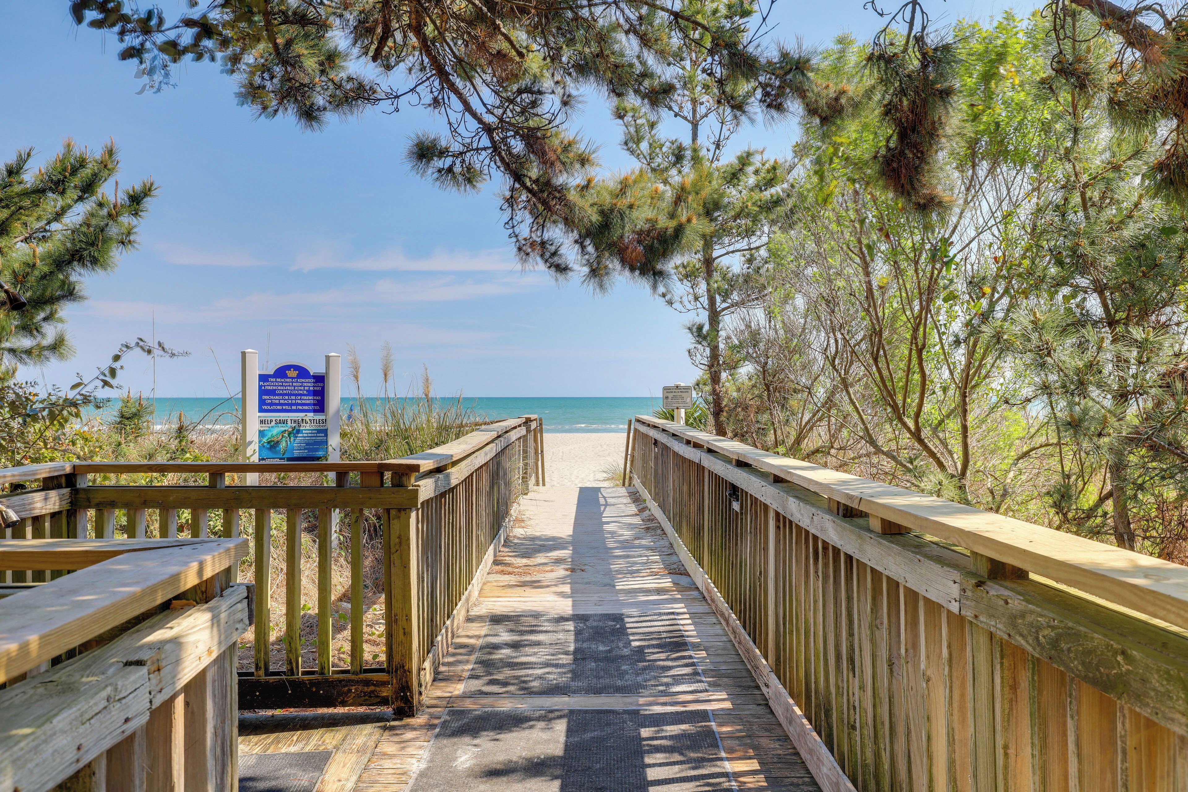 A wooden boardwalk leading to a beach with a signboard.