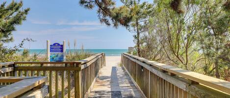 A wooden boardwalk leading to a beach with a signboard.
