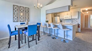 Une cuisine moderne dotée d’un îlot central, de tabourets de bar et d’un coin repas avec des chaises bleues.