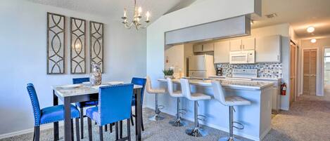 A modern kitchen with a central island, bar stools, and a dining area with blue chairs.