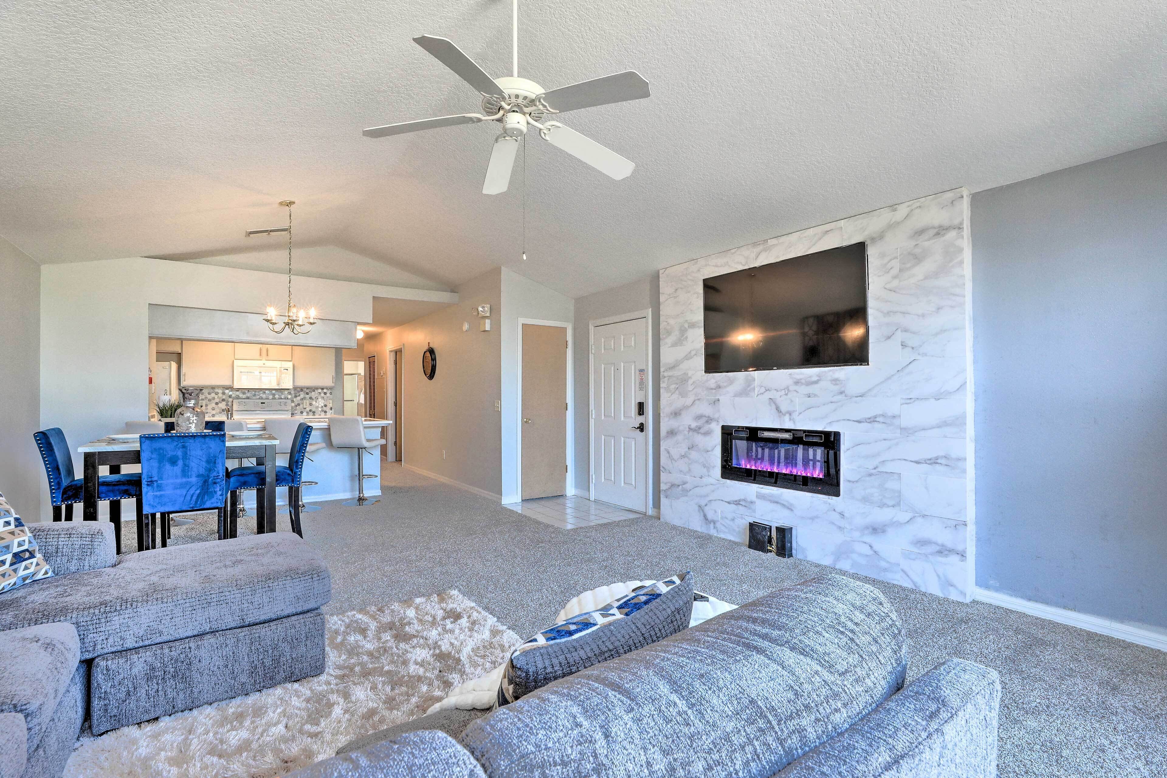 A modern living room with a grey sofa, a ceiling fan, and a flat-screen TV mounted on a marble wall.