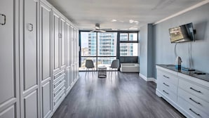 A modern hotel room with a large window, a ceiling fan, a flat-screen TV, and a built-in air conditioning unit. - Beachfront Daytona Studio, Close to Parks! (Daytona Beach Shores)