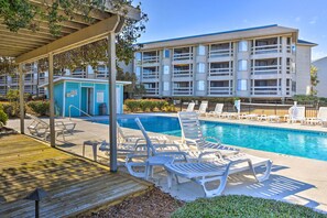 A pool area with lounge chairs and a small building with a sign. - Beachfront Condo w/ 3 Pools on St Helena Island! (Harbor Island)