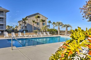 A swimming pool with lounge chairs, palm trees, and a building with multiple floors. - Beachfront Condo w/ 3 Pools on St Helena Island! (Harbor Island)