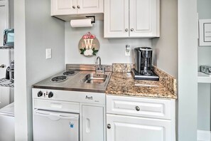 A kitchen with white cabinets, a stove, a sink, and a coffee maker. - Centrally Located Studio w/ Pool in Myrtle Beach (Myrtle Beach)