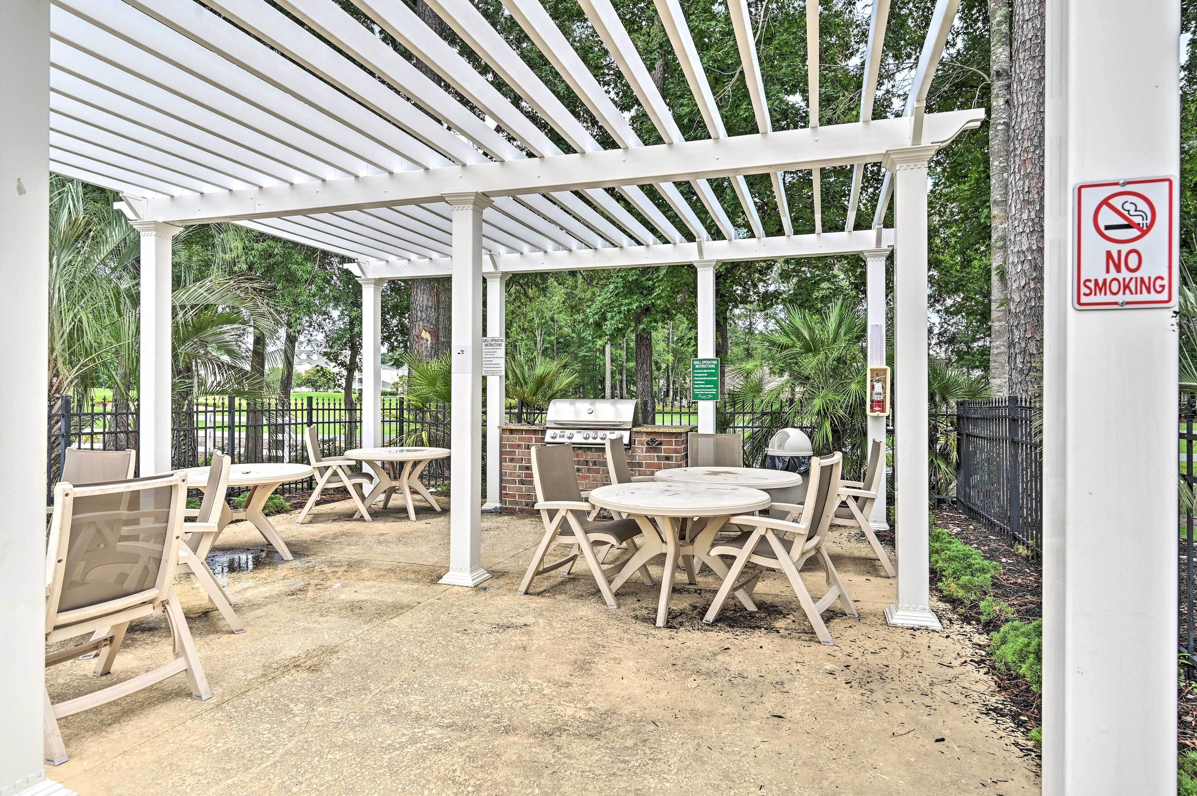 An outdoor patio area with white pergola, tables, chairs, and a barbecue grill.
