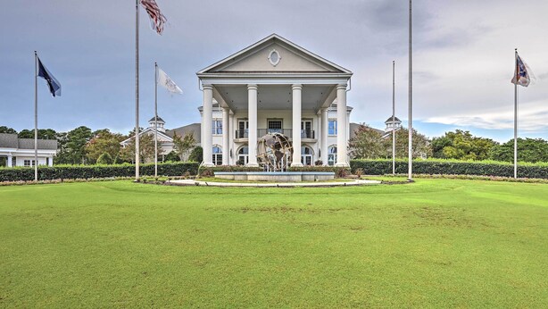 A large, white building with a central entrance and columns, surrounded by a well-maintained lawn and multiple flags.