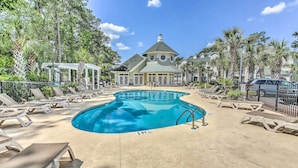 A swimming pool with lounge chairs, a gazebo, and a large building with a distinctive roof.