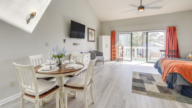 A spacious room with a dining area, a bed, and a large window with curtains. - Baytree Golf Colony Studio ~ 5 Mi to Beach! (Little River)