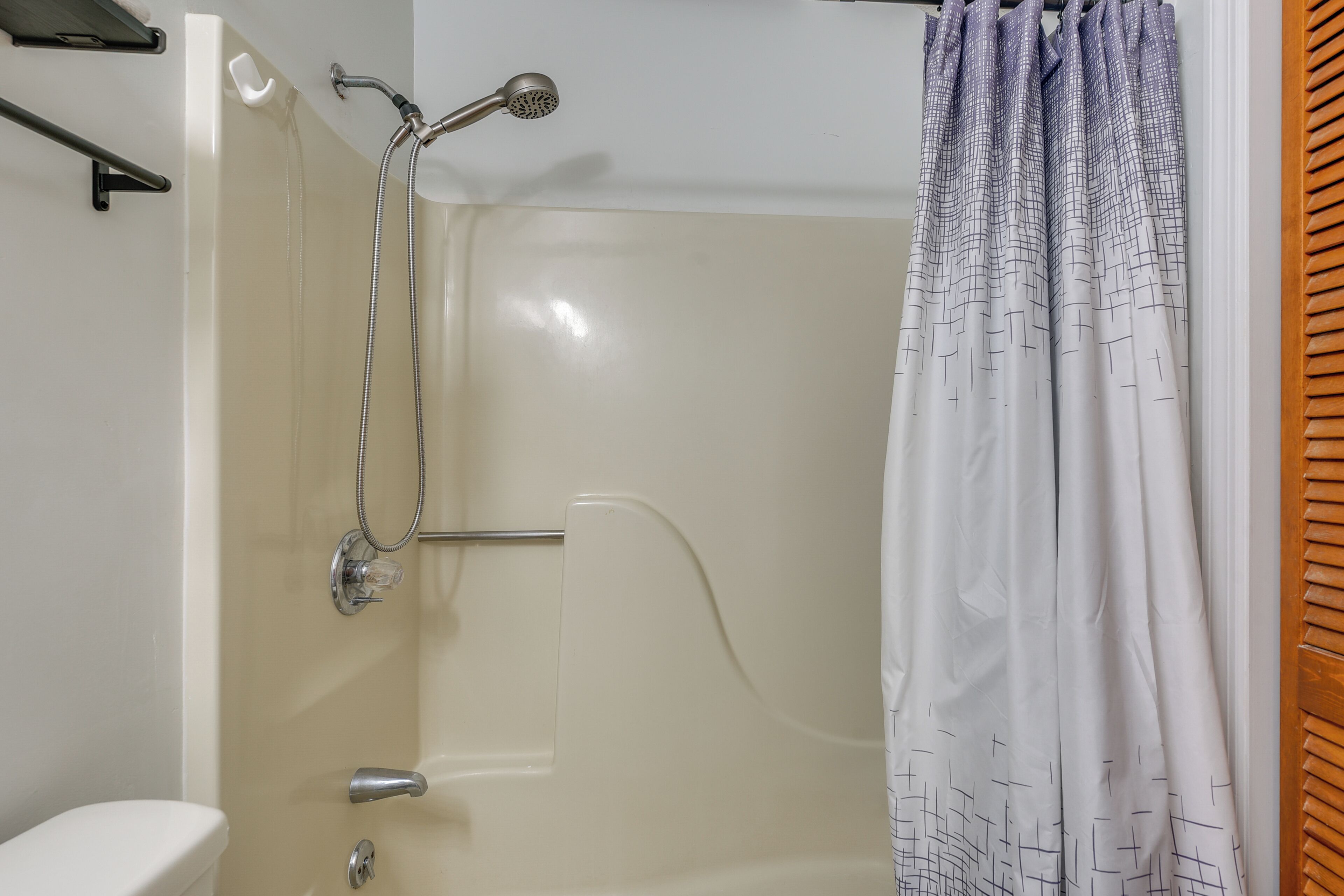 A shower area with a handheld showerhead, a glass-enclosed shower, and a white curtain.