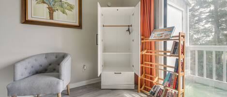 A room with a grey upholstered armchair, a white cabinet with a drawer, and a wooden bookshelf with books.