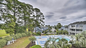 A pool area with a deck, surrounded by palm trees and a fence, with buildings in the background. - Baytree Golf Colony Studio ~ 5 Mi to Beach! (Little River)