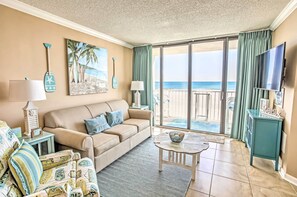 A living room with a beige sofa, a coffee table, and a view of the beach through large sliding glass doors. - 2 Mi to Golfing: Oceanfront Myrtle Beach Condo (Myrtle Beach)