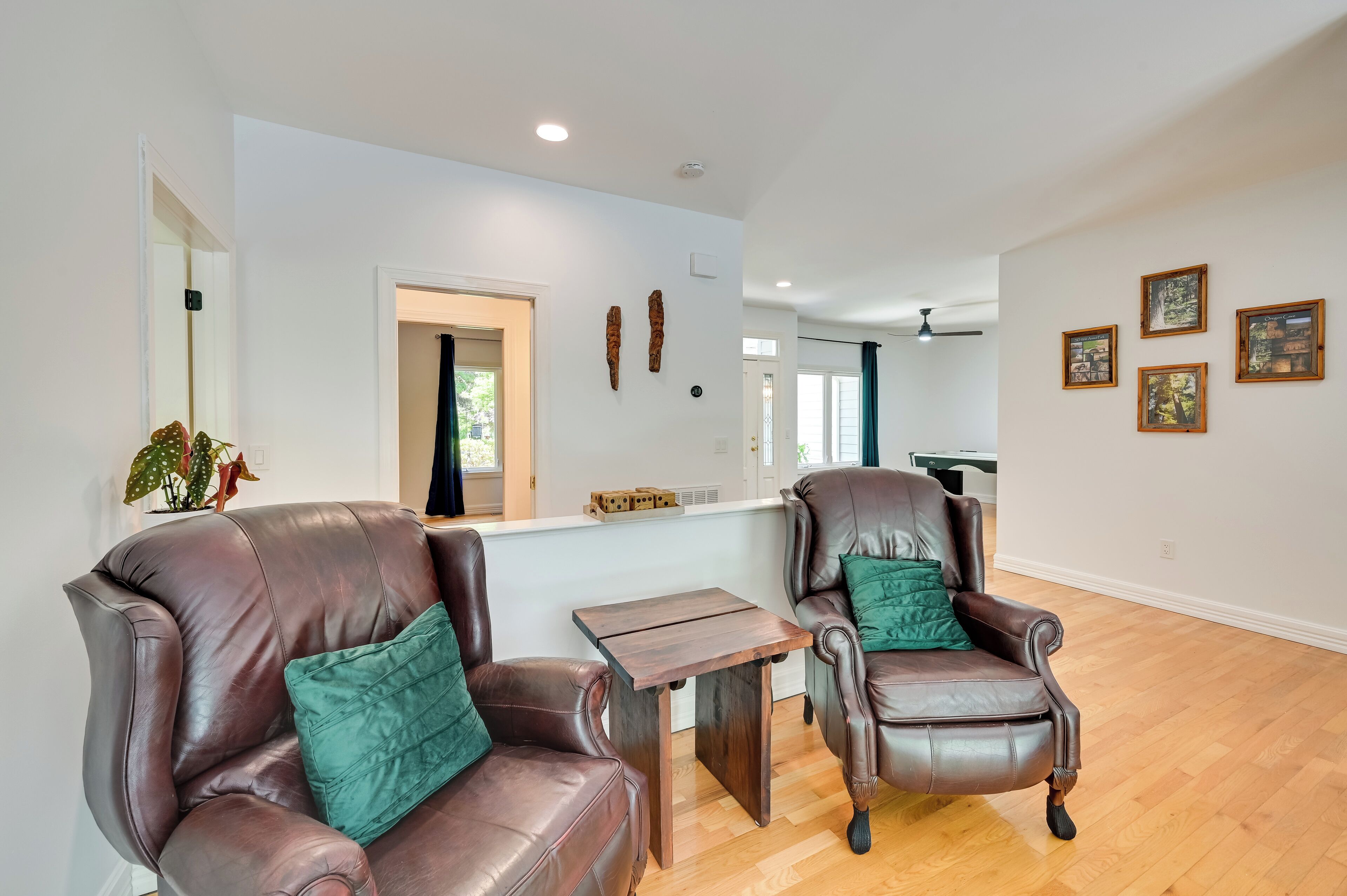 A spacious living area with two leather armchairs, a small wooden table, and a white wall with framed pictures.