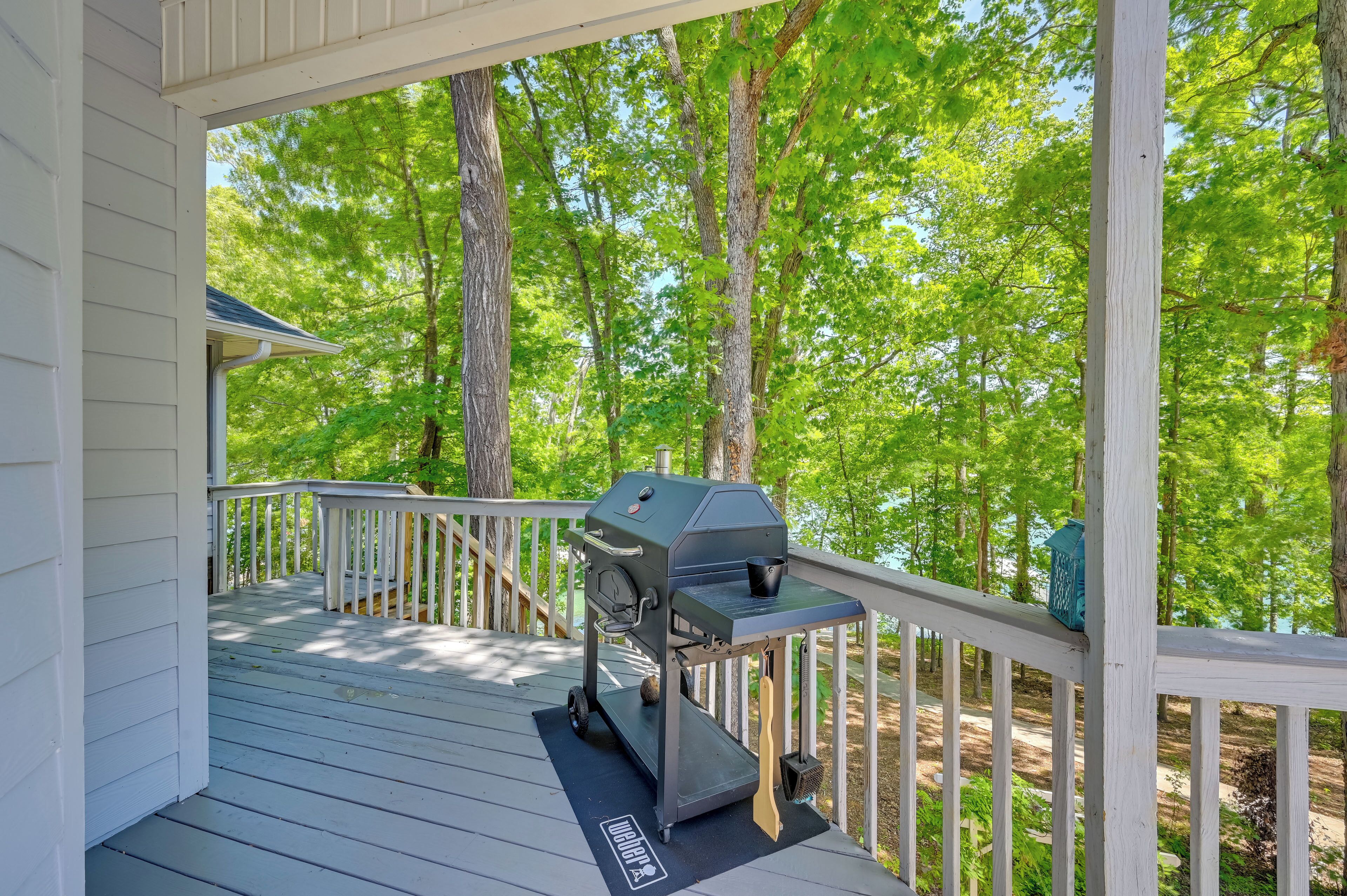 A covered deck with a grill, surrounded by trees.