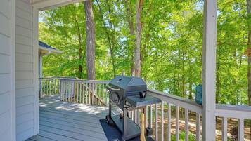 A covered deck with a grill, surrounded by trees.