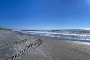 A beach with footprints leading to the water, a clear sky, and distant buildings. - 2 Mi to Barefoot Landing! 'bailey's Beach Cottage' (North Myrtle Beach)