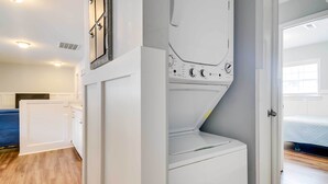 A laundry room with a washing machine and dryer, a blue sofa, and a bed in the adjacent room. - 2 Mi to Barefoot Landing! 'bailey's Beach Cottage' (North Myrtle Beach)