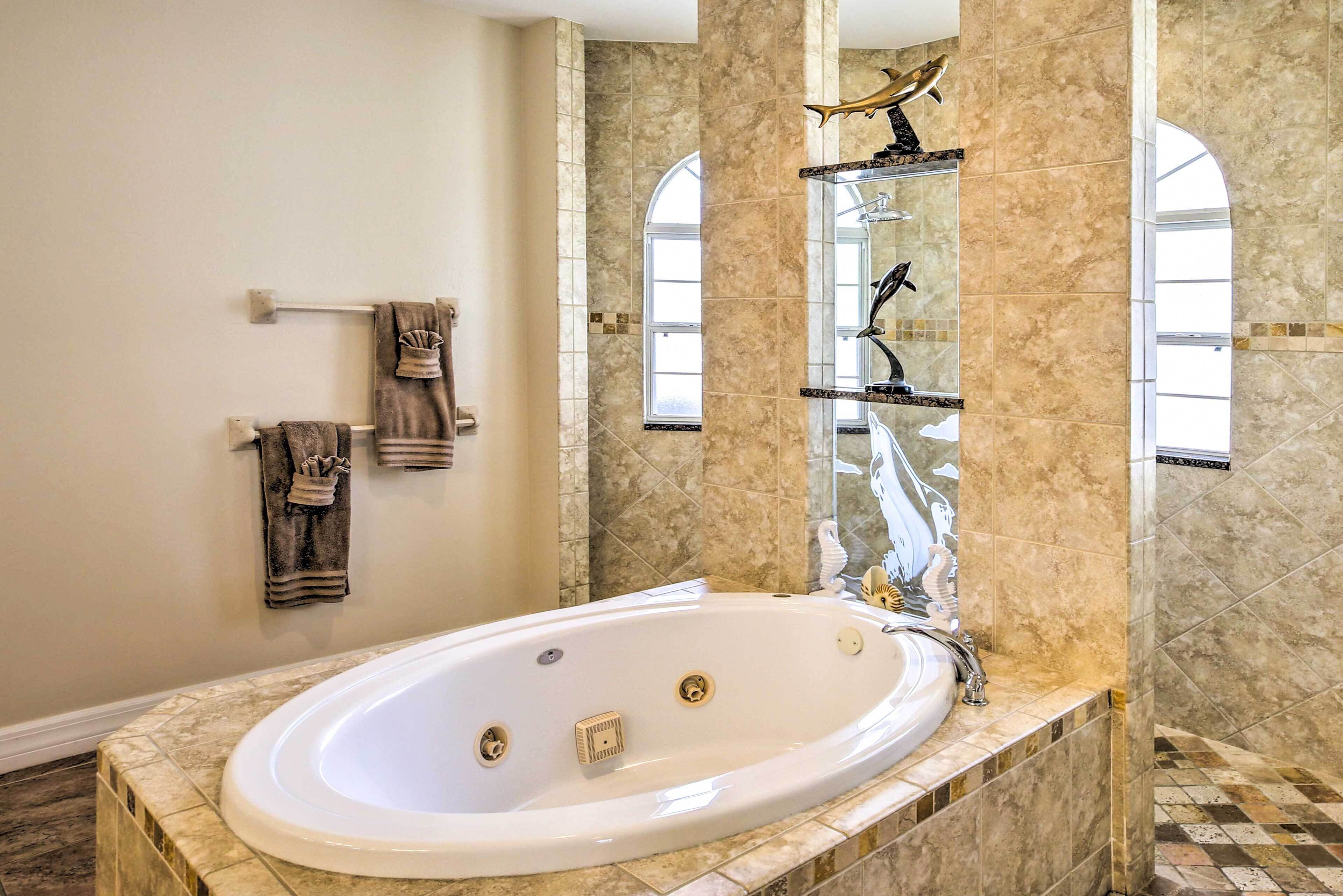 A spacious bathroom with a large bathtub, marble walls, and a window providing natural light.