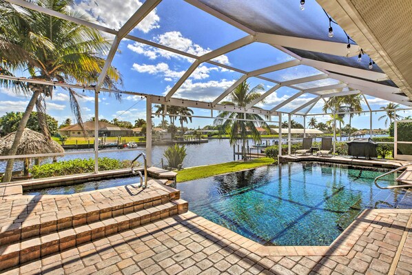 Relax by the serene pool surrounded by palm trees and a thatched-roof hut.