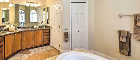 A bathroom with a large bathtub, wooden cabinets, a vanity with a mirror, and a towel rack.