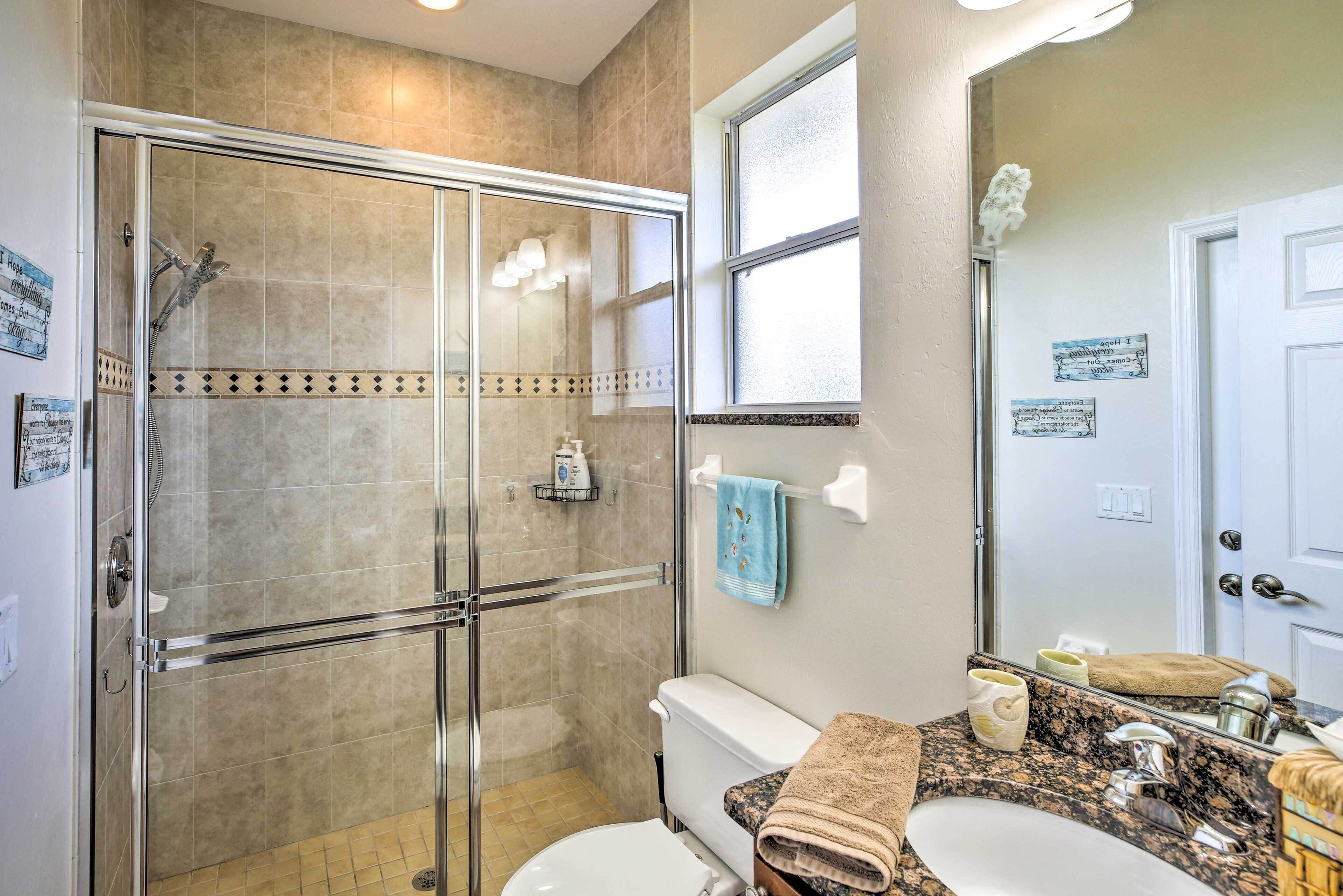 Un baño con ducha envuelta en vidrio, inodoro, lavamanos y tocador con espejo.