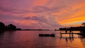 A sunset over a calm lake with a dock and chairs.