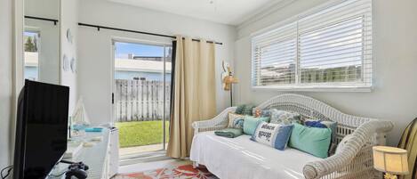 A bedroom with a bed, a TV, a gaming console, and a window with blinds.
