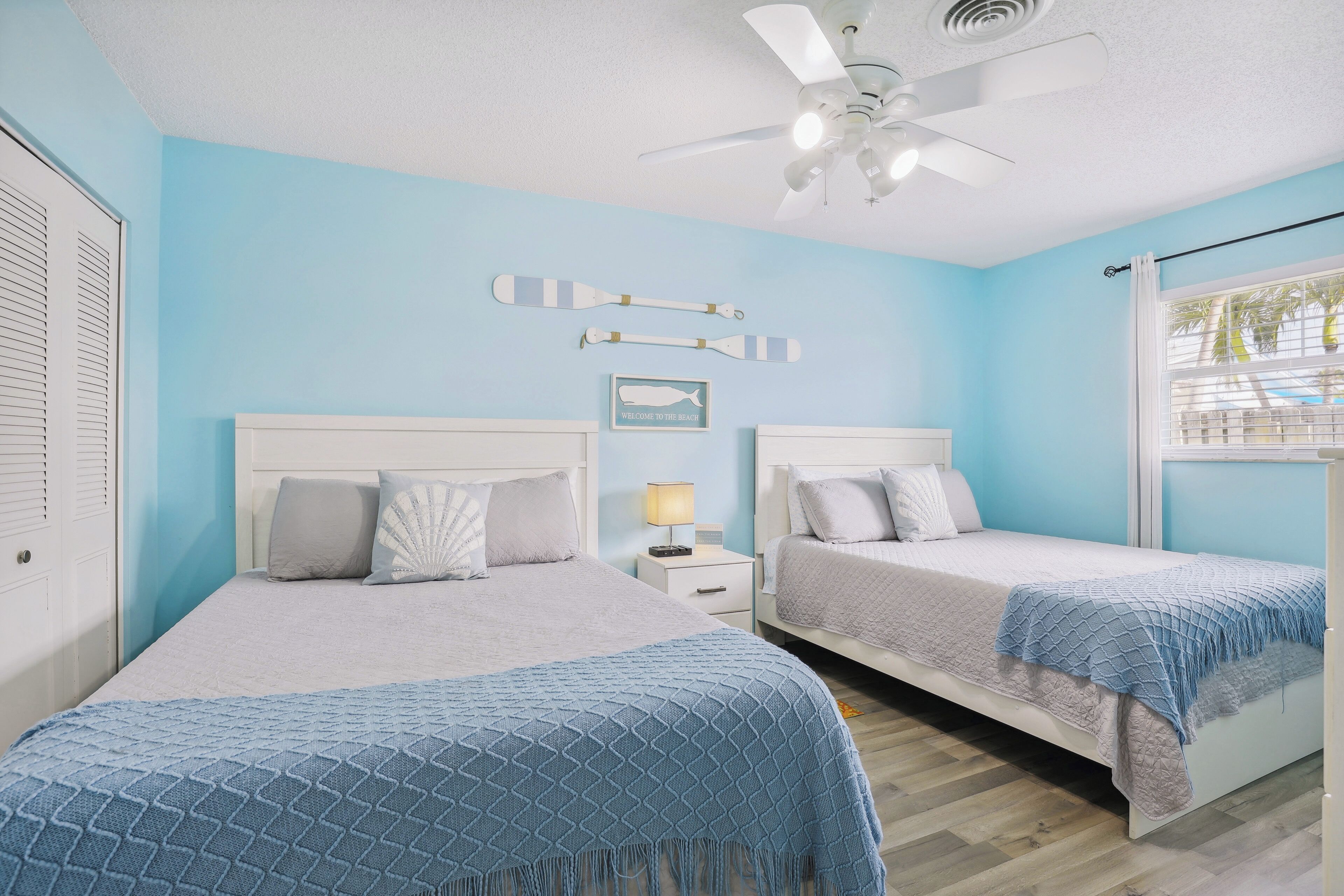 A bedroom with two beds, a ceiling fan, and a window with blinds.