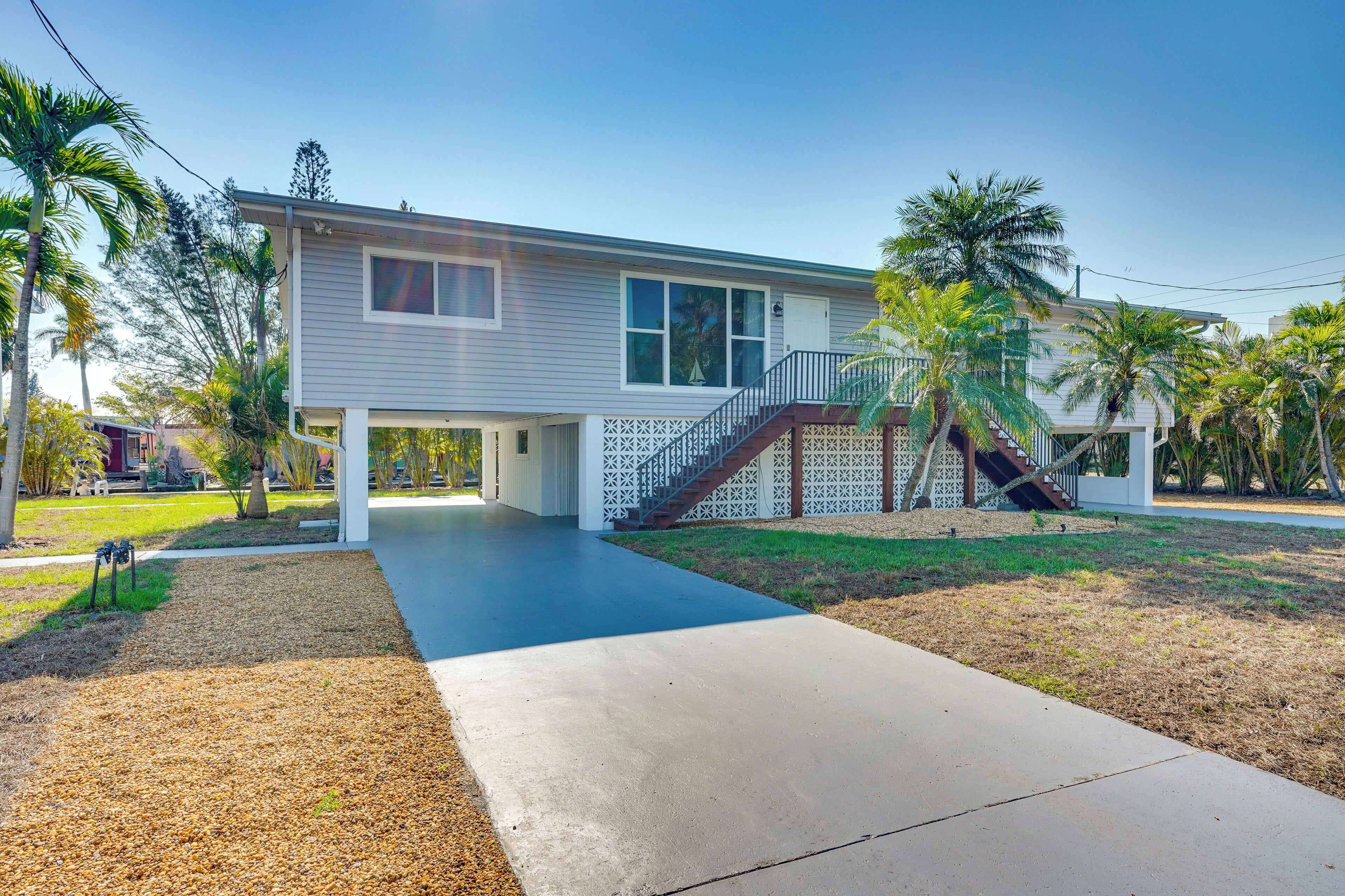 A two-story house with a covered porch, a staircase, and a front yard with palm trees.