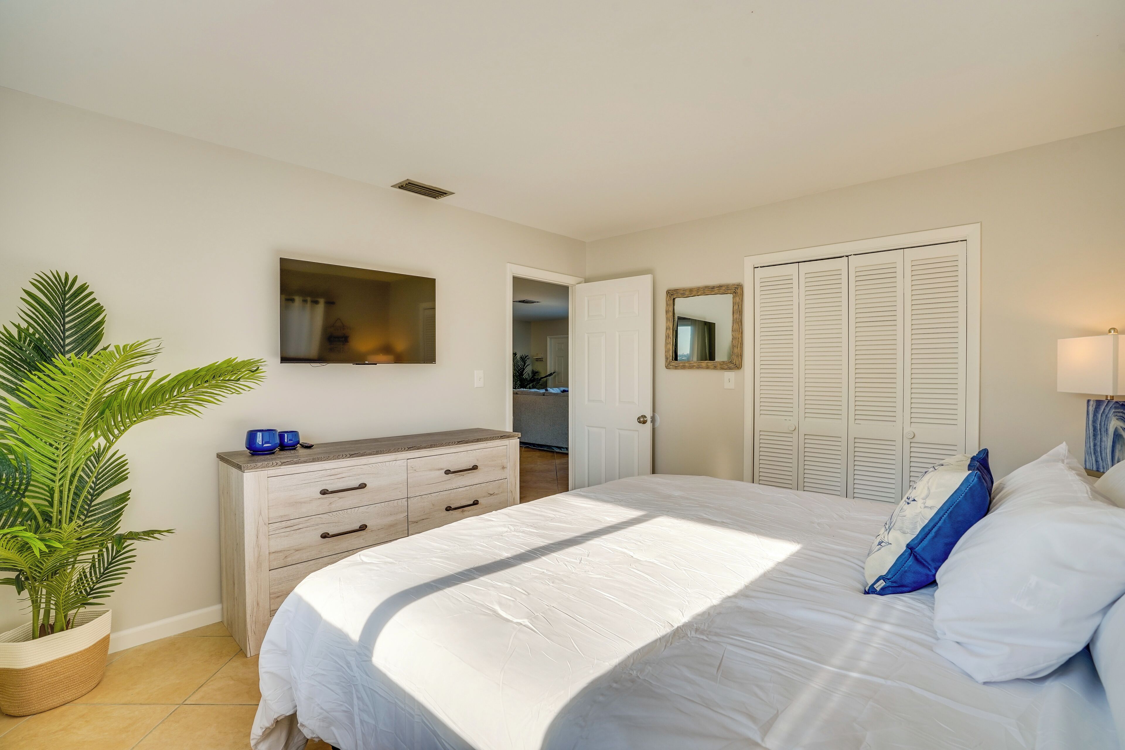 A bedroom with a bed, a dresser, a mirror, and a potted plant.