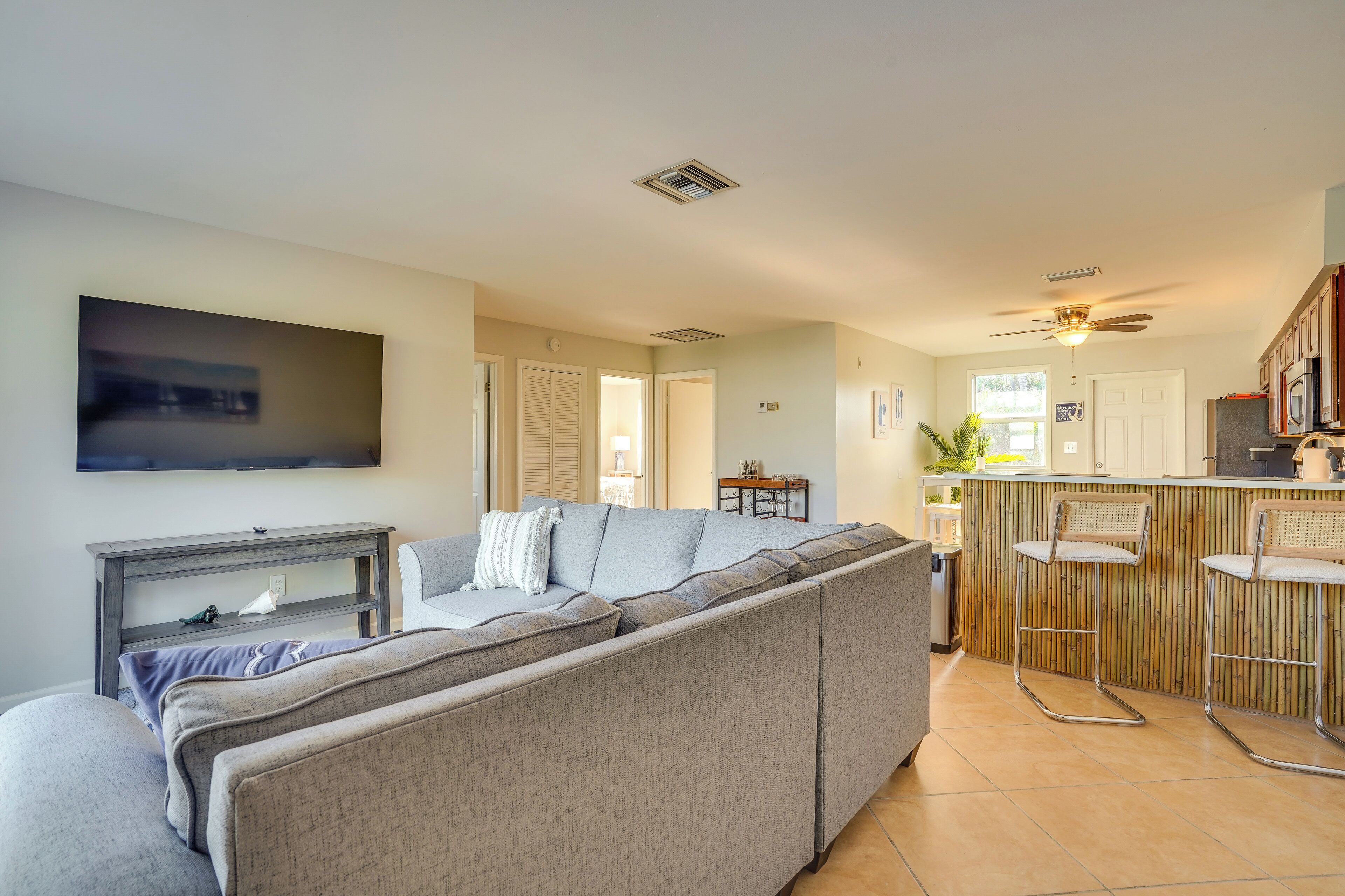 A modern living room with a sectional sofa, a flat-screen TV, and a kitchen area with a bar stool.
