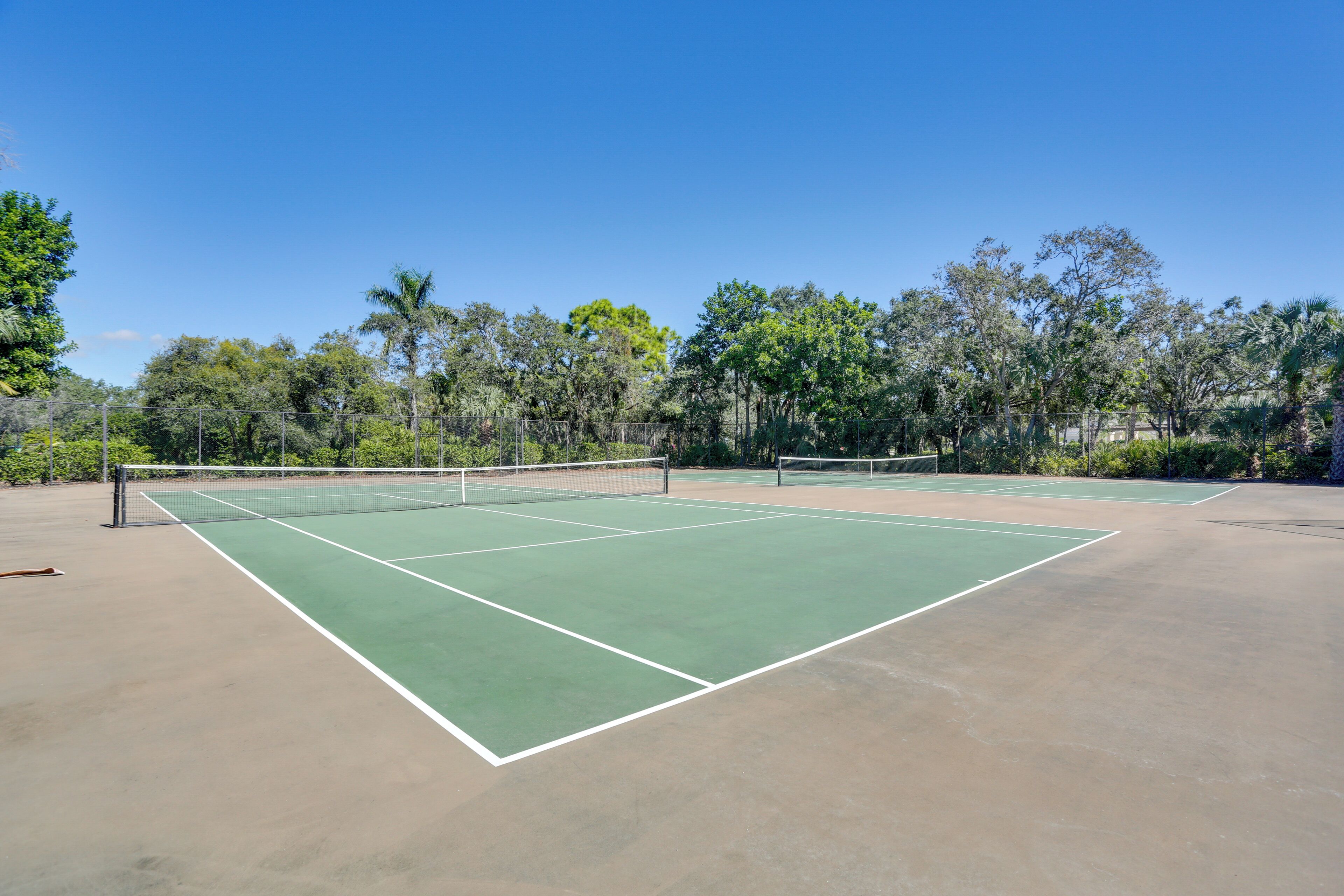 A tennis court with a net in the center, surrounded by trees and a clear sky.
