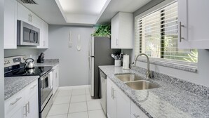 A modern kitchen with white cabinets, a stainless steel refrigerator, a built-in oven, and a granite countertop. - Bonita Springs Vacation Rental w/ Community Pool! (Bonita Springs)
