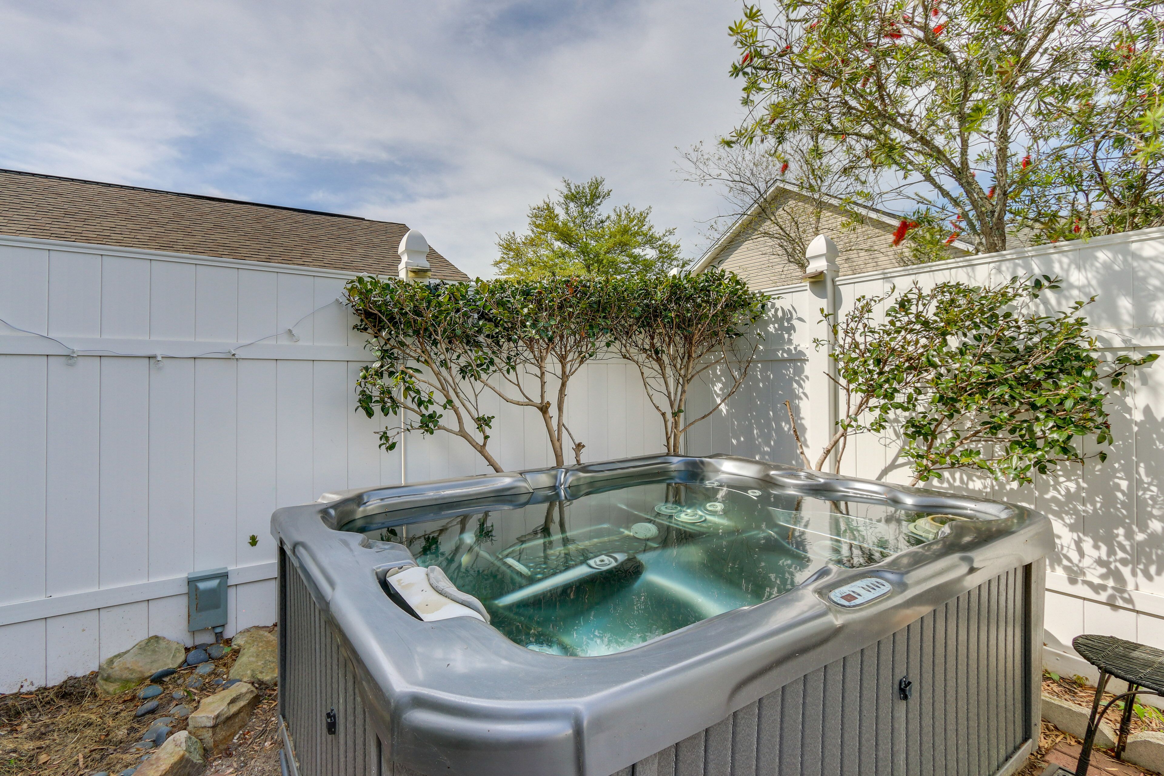 Un bain à remous dans un jardin, avec une clôture blanche, des arbres et un ciel dégagé.