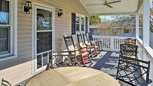A covered porch with wooden chairs and a table, a ceiling fan, and a view of the surrounding trees. - Canalfront Surfside Beach Home - Walk to Beach! (Surfside Beach)